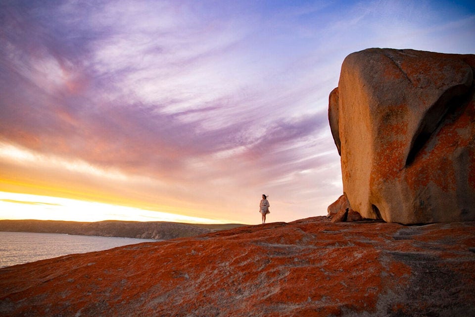 Woman standing on large rocks at foreshore with evening sky and clouds
